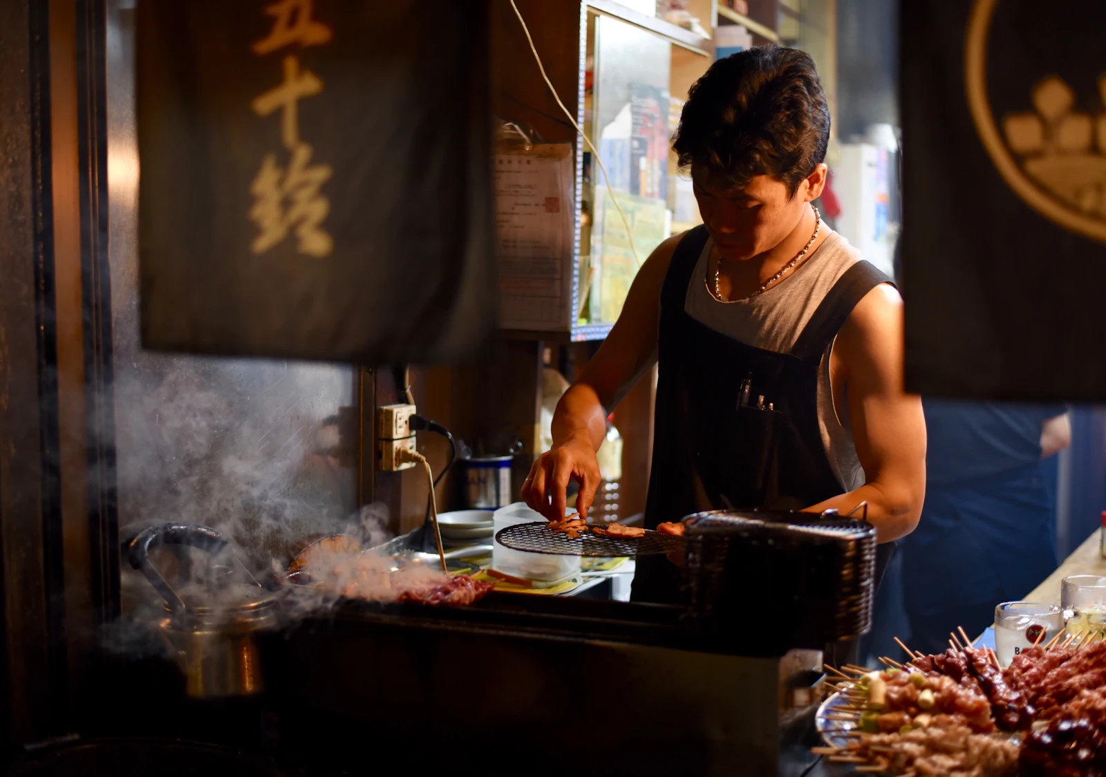 焼き台の前で串を返す手元。煙が立っている